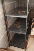 Front view of metal storage shelf showing four shelves with rust spots and wear.