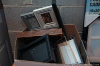 Various picture frames stacked in a box in different sizes and styles including wood-tone and black with white stitching.