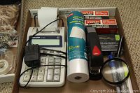Photo of Sharp EL-2192 printing calculator with paper roll, power adapter, Staples boxes of staples, a black stapler and roll of paper in a box