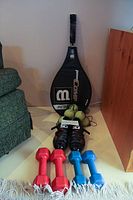 Full lot arrangement showing dumbbells, bike shoes, tennis racket with cover, and tennis balls.