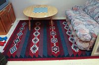 Full view of the rectangular Polonaise patterned rug placed under a wooden oval table and next to a couch, showing overall color and design.