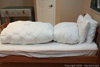 Overview of two folded white duvets and two pillows on wooden daybed