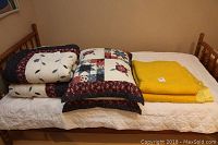Overview of the bedding items on a wooden bed: two folded patchwork quilts with matching pillows and two yellow wool blankets.