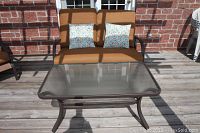 Overall view of metal framed loveseat with cushions, pillows and matching glass-top table on wooden deck