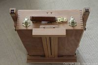 Top view of folded wooden easel showing brass clasps, leather handle, and wood grain finish.