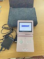 Console, charger and felt case with system powered on at Game Boy splash screen
