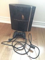 Front view of PlayStation 3 console standing upright with controller and power cord