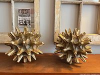 Two gold resin spiked orb sculptures on wooden surface