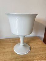 Full view of white milk glass pedestal vase on wood surface