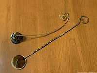 Two candle snuffers on tabletop showing overall size, shape and handles