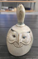 Front view of beige tan glazed ceramic bell with owl motif and handle