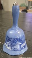 Full view of blue and white porcelain bell showing scenic cottage pattern and silver-tone finial