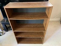 Front view of brown engineered wood bookcase showing four shelves and overall condition