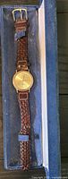 Full watch in blue presentation box showing gold-tone case and braided strap