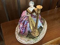 Front view of porcelain figurine showing woman with harp and detailed gown