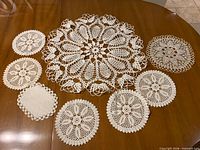 All eight white/cream cotton crocheted lace doilies laid out on table showing size differences and patterns.