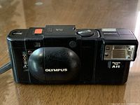 Front view of Olympus XA camera with closed clamshell and attached A11 flash