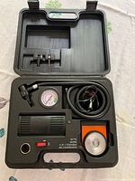 Open storage case showing compressor, gauge, hose, power cord, adapters