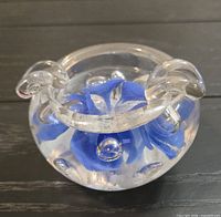 Angle showing clear glass paperweight with blue flower, handles, bubbles