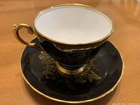 Teacup resting on saucer showing exterior color, gilded floral pattern and trim