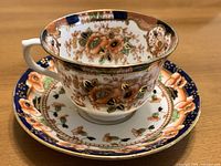 Teacup on saucer showing floral design, cobalt border and gilt accents