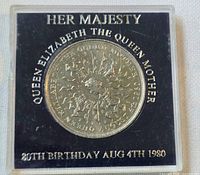 Reverse of coin in holder showing Queen Mother 80th Birthday legend and floral design