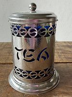 Front view of metal tea canister showing “TEA” cutout and blue liner