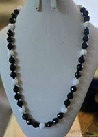 Full view of necklace on display bust showing alternating black and white faceted beads