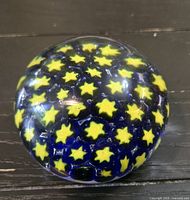 Full view of spherical glass paperweight showing yellow star motif