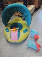 Inflatable baby pool float with canopy, steering wheel, and arm bands displayed on floor