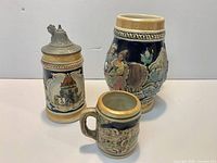 Three ceramic beer steins: one lidded, one wide-body, one miniature