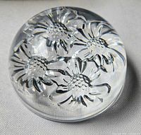 Top view of clear glass paperweight showing four raised daisy flowers