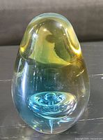Front view of teardrop-shaped glass paperweight showing blue and yellow internal swirl and bubble inclusion