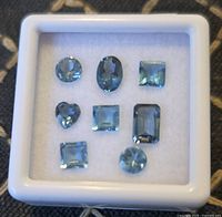 Front view of display box showing eight faceted blue topaz gemstones