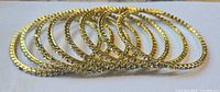 Eight gold-tone metal bangles with rhinestones laid side by side on white surface