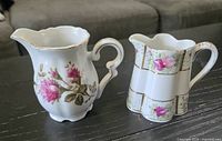 Front view of both porcelain creamers displaying rose decorations and gold trim