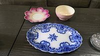 Three porcelain pieces on table: blue & white platter, pink bowl, flower saucer