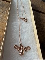 Necklace laid out in box showing bee pendant and chain