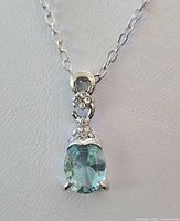 Close-up of pendant showing oval faceted blue stone, clear accents, and silver-tone setting