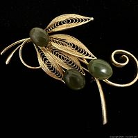 Front view of gold-tone filigree leaf brooch showing three green cabochon stones