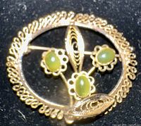 front view of gold-tone filigree brooch showing green cabochon stones and floral design