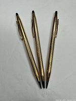 Three gold-tone Cross ballpoint pens laid out