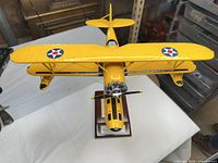 Overhead frontal view showing yellow biplane wings, U.S. star roundels, radial engine and propeller, and display stand
