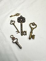 Overview of five decorative brass key charms on white background