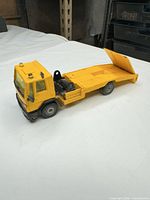 Left side view of yellow flatbed truck with ramp lowered