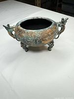 Side view showing overall form, dragon handles, tripod legs, verdigris patina