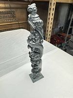 Front view of full carved stone totem pole on square base