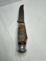 Full view of knife showing blade shape, carved antler handle and aluminum pommel