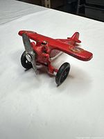 Three-quarter front view of red cast iron airplane showing propeller, wheels, overall form