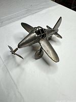 Oblique front view of silver metal airplane sculpture showing propeller, wings and landing gear